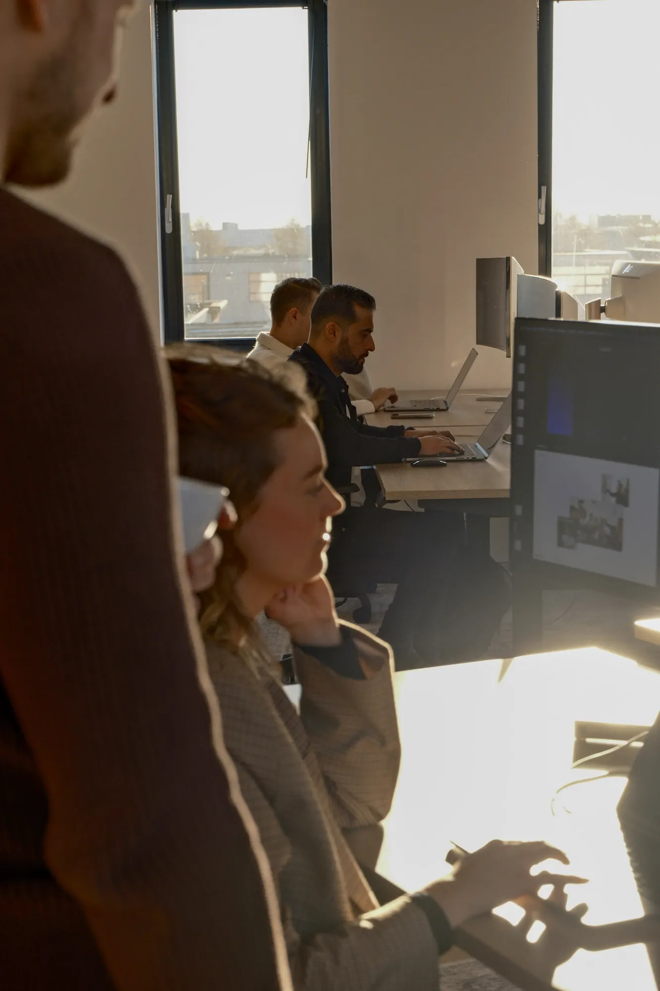 Moderne kantoorruimte met vrouw en drie mannen die achter laptops werken bij grote ramen.